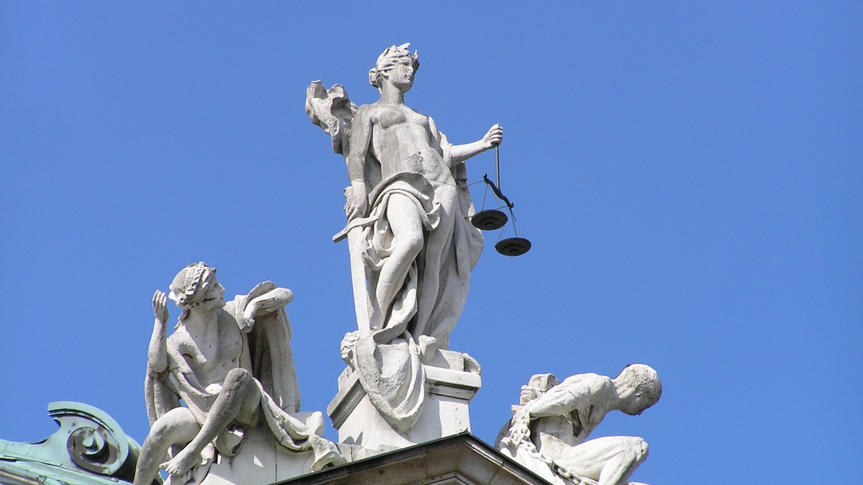 Ausschnitt von Statuengruppe „Gerechtigkeit“ von Balthasar Schmitt, bestehend aus Justitia mit Waage und Schwert, sowie Unschuld (links) und Laster (rechts), auf dem Südgiebel des Justizpalastes in München | Foto: wikimedia commons (CC BY-SA 3.0)